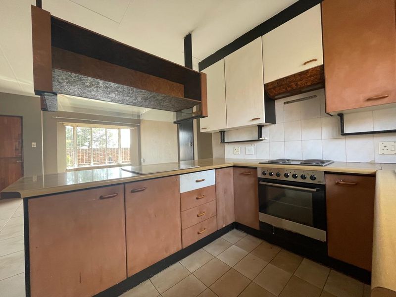 A dated kitchen featuring built-in cabinetry, an electric oven and hob, tiled backsplash, and tiled flooring, offering potential for modernization.