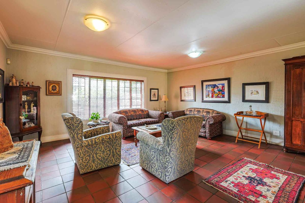 A spacious living room featuring terracotta floor tiles, large windows with fitted blinds, and classic ceiling cornicing.
