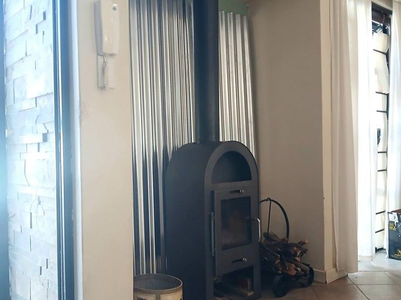 Living area featuring a modern freestanding fireplace with a flue pipe, set against a corrugated metal feature wall and stone-clad pillar.