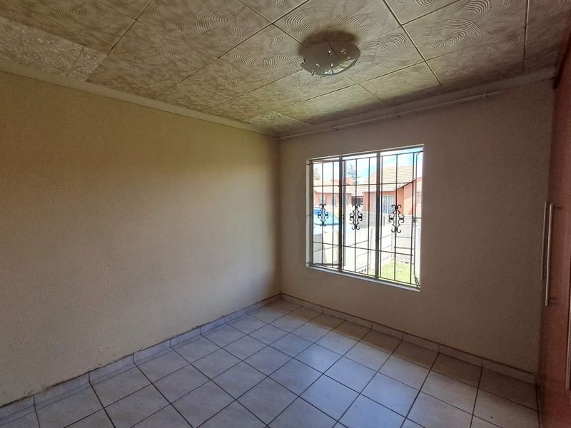 An empty bedroom featuring tiled flooring, security bars on the window, and a built-in cupboard, offering a blank canvas for renovation.