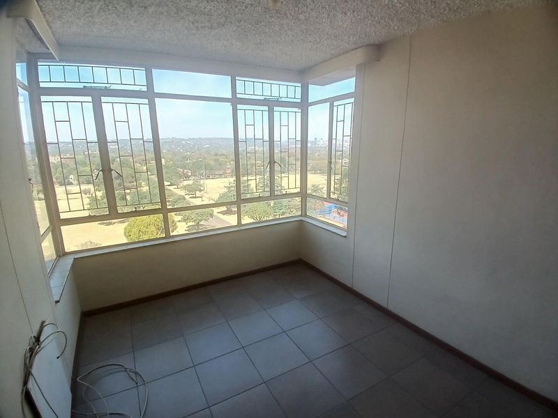 An enclosed balcony or sunroom featuring large windows with expansive views, tiled flooring, and a textured ceiling, offering a bright and versatile space.
