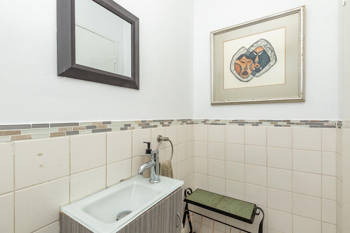 A compact bathroom featuring a wall-mounted vanity with a modern basin, tiled walls with decorative mosaic accents, and a framed wall mirror.
