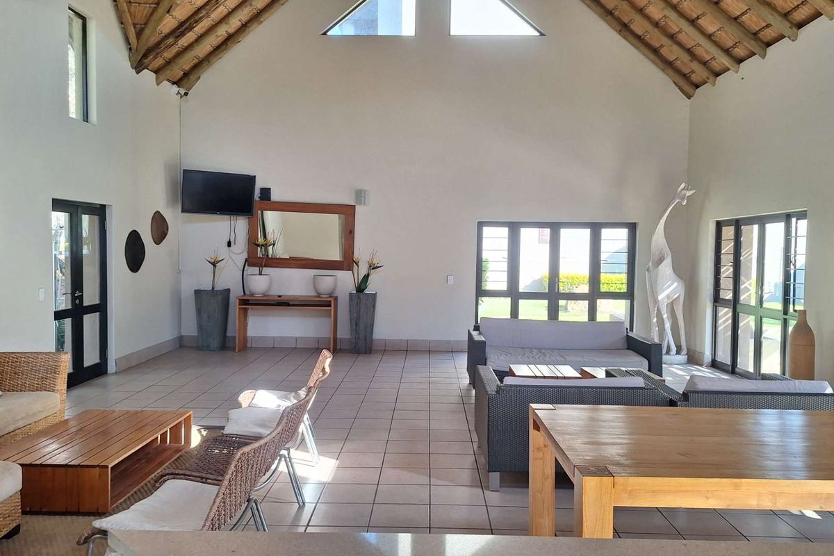 Spacious living area featuring a high vaulted thatched ceiling with exposed timber trusses, tiled flooring, and large windows providing ample natural light.