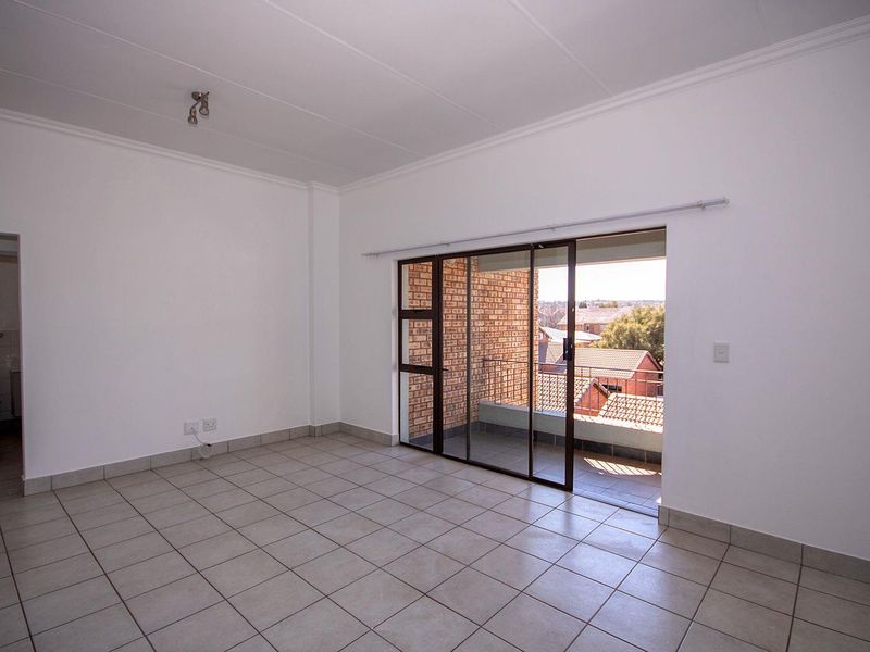An empty, neutrally finished living area featuring tiled floors and a sliding glass door providing access to a private balcony.