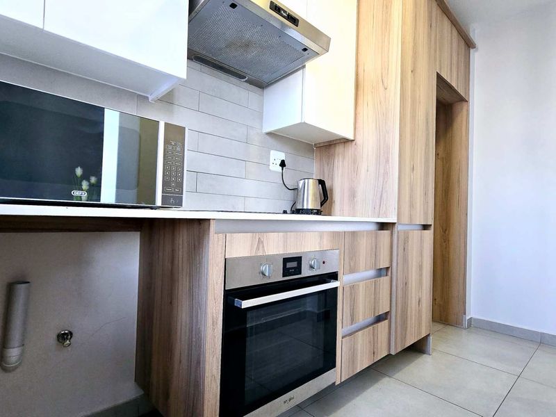 Modern kitchen featuring light wood-finish cabinetry, stone countertops, built-in oven, extractor fan, and neutral tiled backsplash in a clean, contemporary layout.