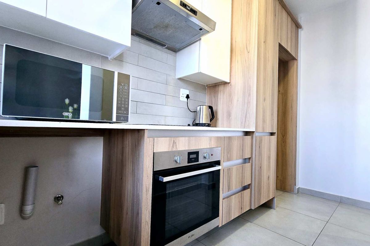 Modern kitchen featuring light wood-finish cabinetry, stone countertops, built-in oven, extractor fan, and neutral tiled backsplash in a clean, contemporary layout.