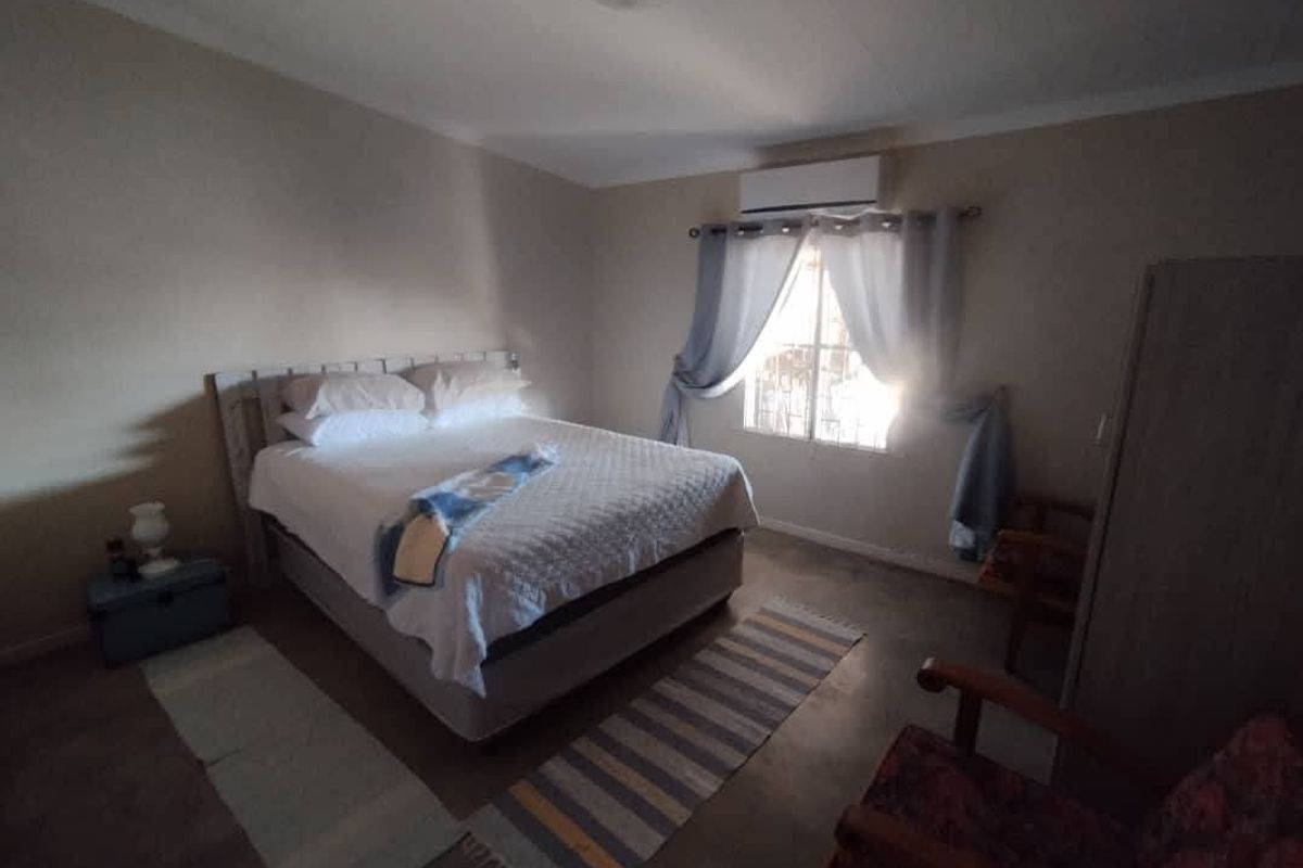 A functional bedroom featuring a wall-mounted air conditioning unit and a window with security bars, providing a comfortable and practical living space.