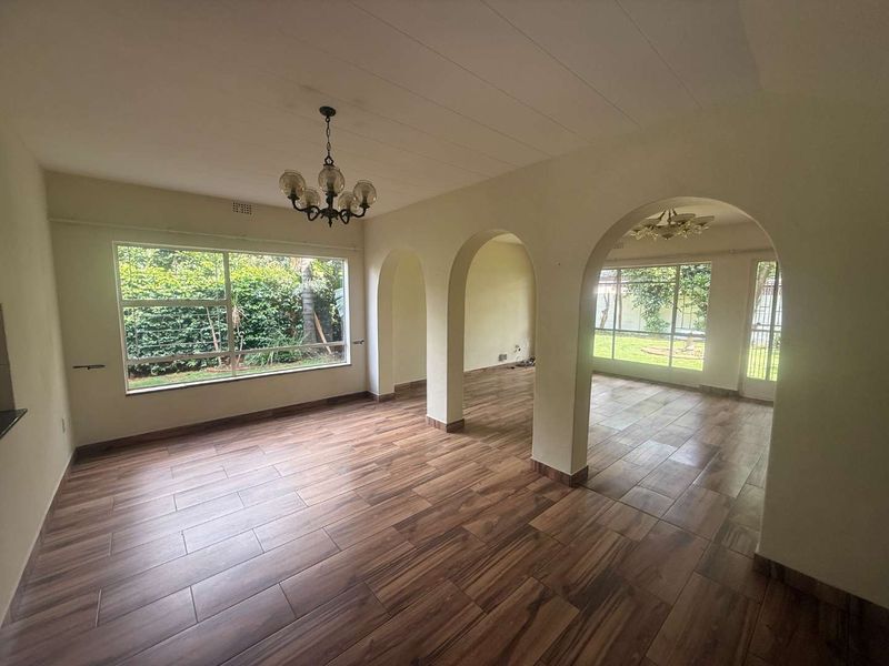 Spacious, light-filled living area featuring wood-look tile flooring, distinctive arched architectural details, and large windows overlooking the garden.