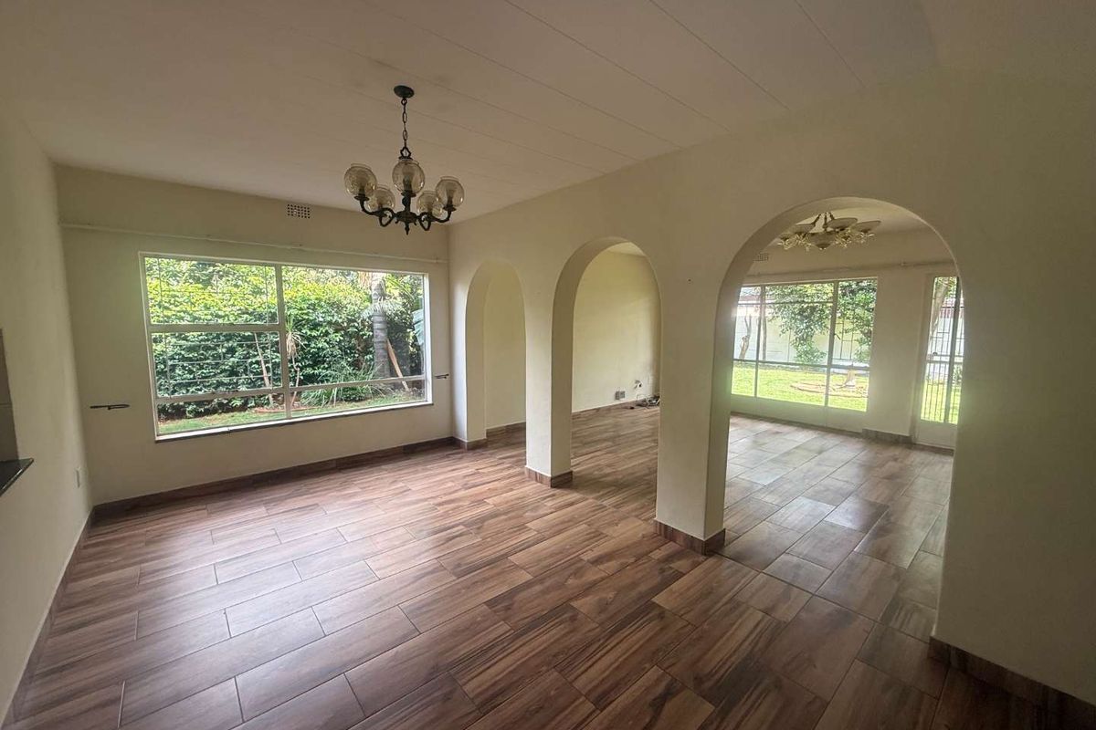 Spacious, light-filled living area featuring wood-look tile flooring, distinctive arched architectural details, and large windows overlooking the garden.