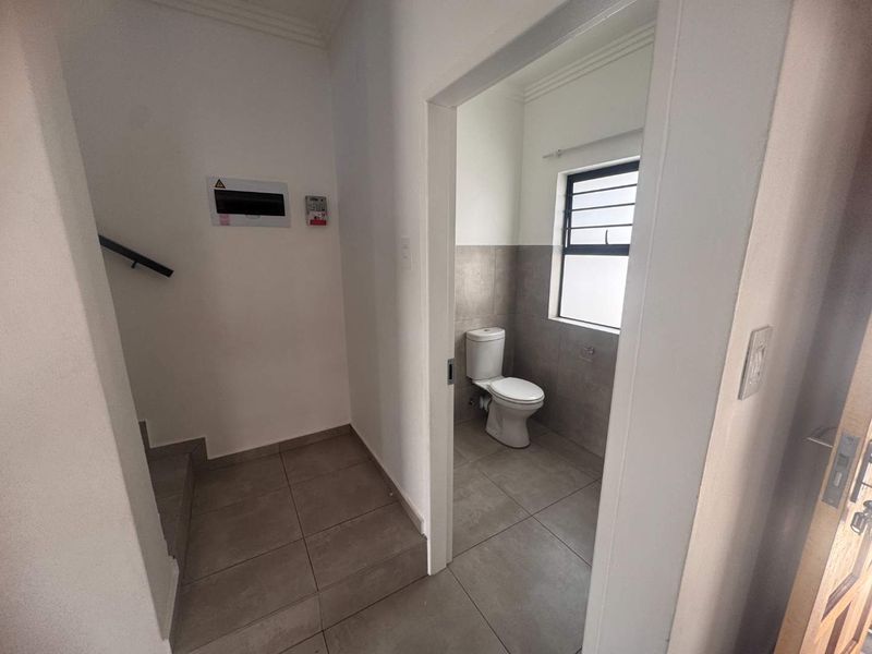 A functional guest bathroom featuring tiled finishes and a toilet, located adjacent to the staircase area.