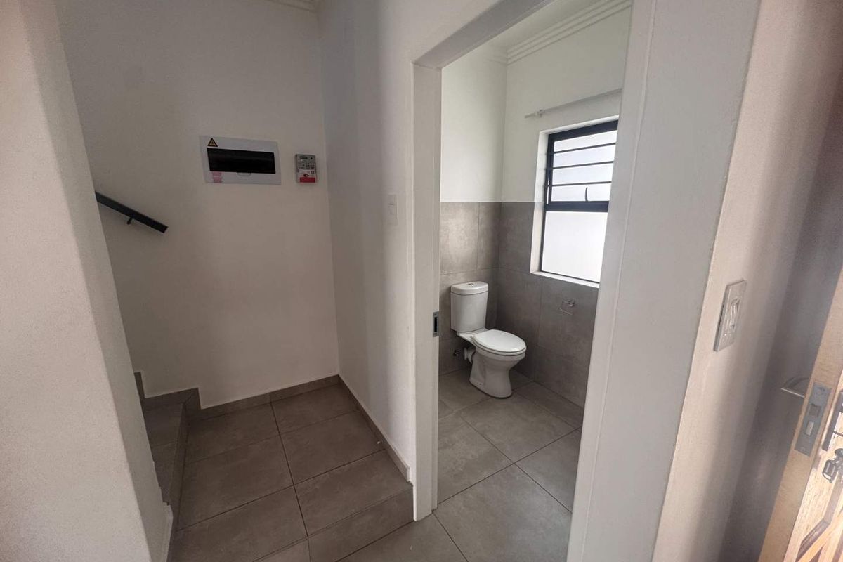 A functional guest bathroom featuring tiled finishes and a toilet, located adjacent to the staircase area.