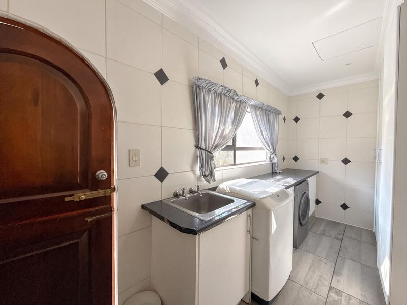 A functional laundry room featuring tiled walls, granite countertops, a stainless steel sink, and dedicated space for laundry appliances.