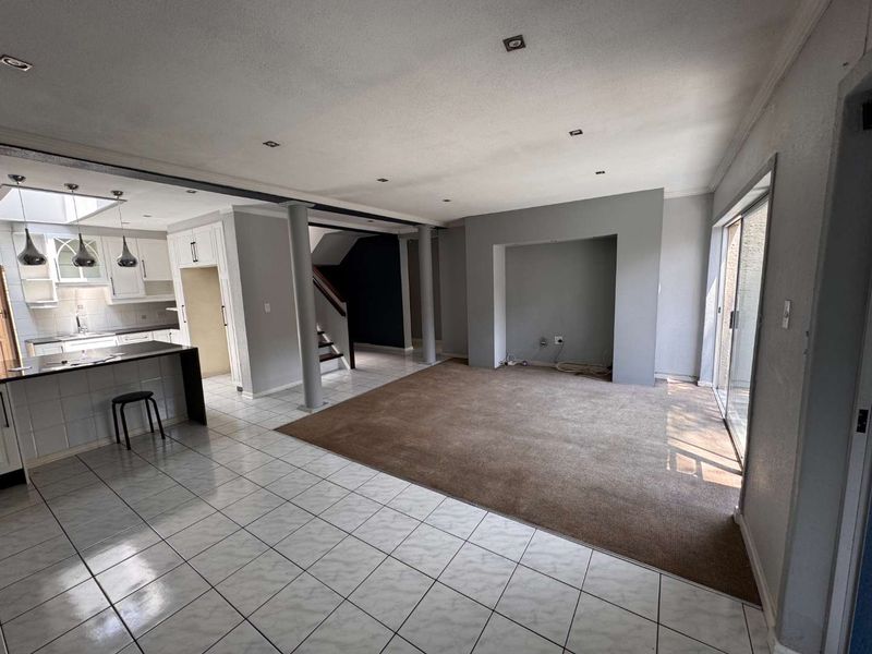 Spacious open-plan living and kitchen area featuring tiled and carpeted flooring, recessed lighting, and direct access to the outdoors via sliding glass doors.
