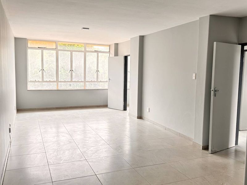 A spacious, empty living area featuring neutral tiled flooring and large windows that provide ample natural light.
