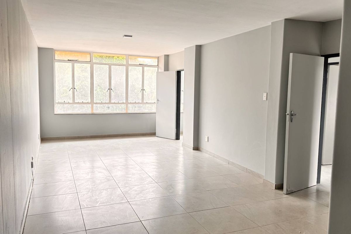A spacious, empty living area featuring neutral tiled flooring and large windows that provide ample natural light.