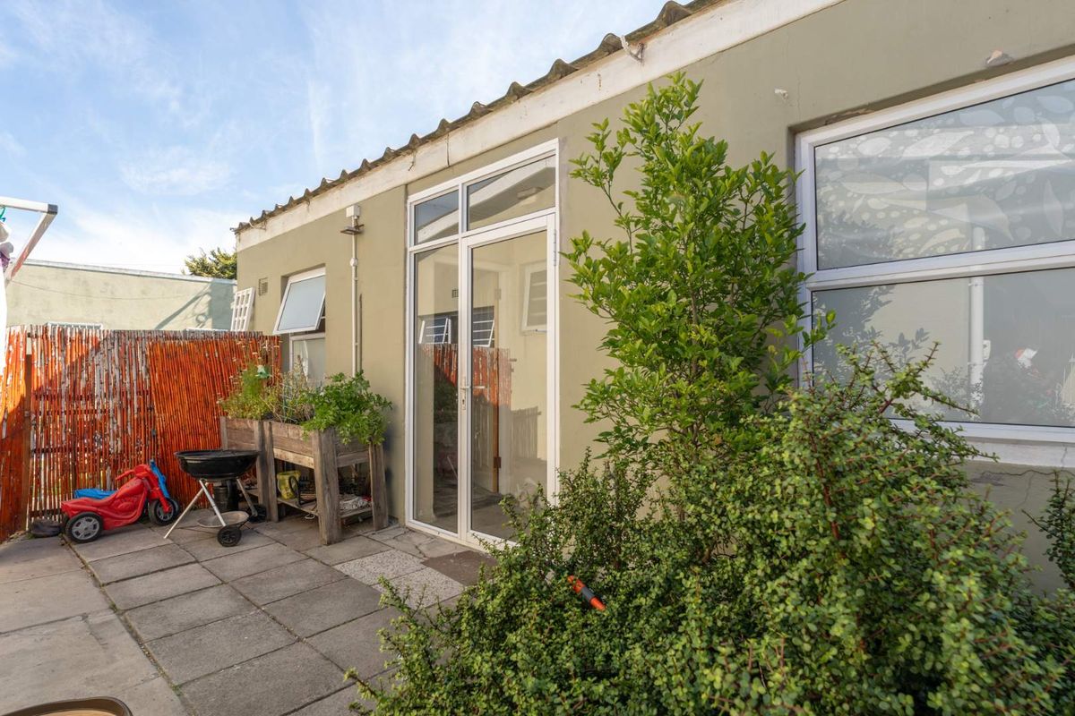 Rear exterior view of the property featuring a paved patio area, glass sliding doors, and established garden greenery.