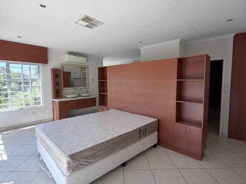 Spacious bedroom featuring tiled flooring, a built-in vanity with double basins, and a central wooden room divider with integrated shelving.