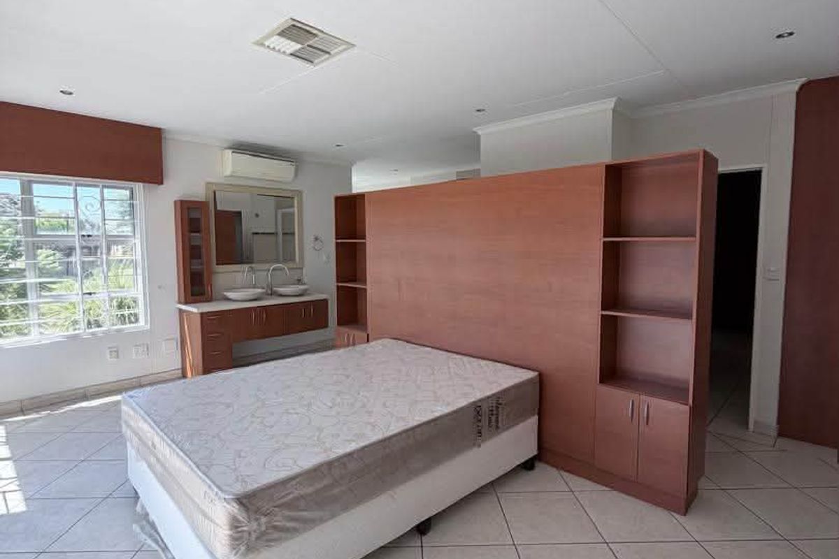 Spacious bedroom featuring tiled flooring, a built-in vanity with double basins, and a central wooden room divider with integrated shelving.