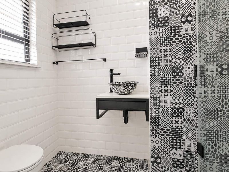 Modern bathroom featuring subway wall tiles, patterned floor and shower tiles, a floating vanity with a vessel sink, and a glass shower enclosure.