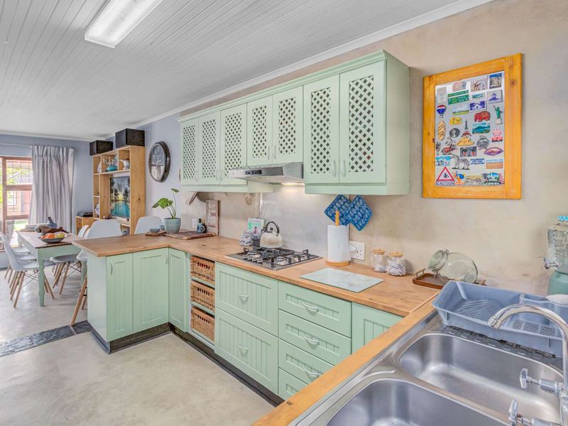 Open plan kitchen featuring light green cabinetry, wooden countertops, a gas hob, extractor fan, and a double stainless steel sink.