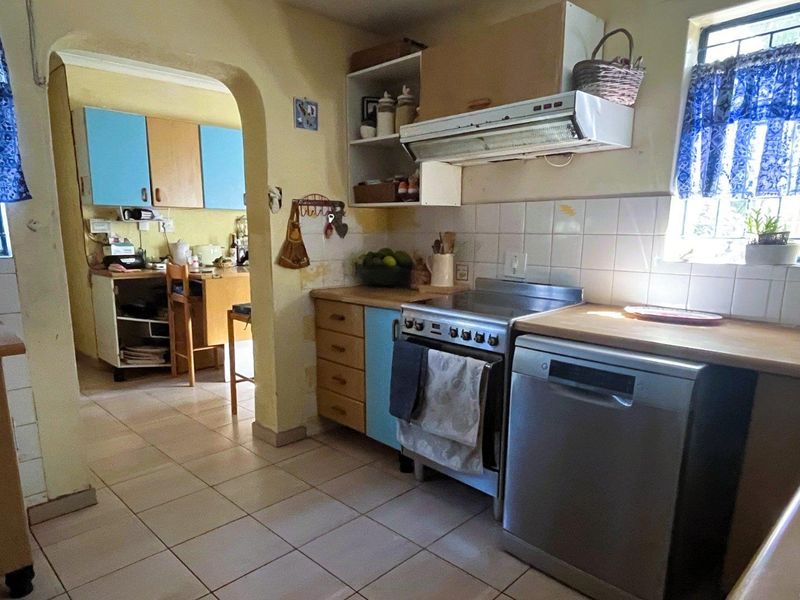A functional kitchen featuring tiled flooring, built-in cabinetry, and an extractor fan, with an open archway leading to an adjacent utility or prep area.