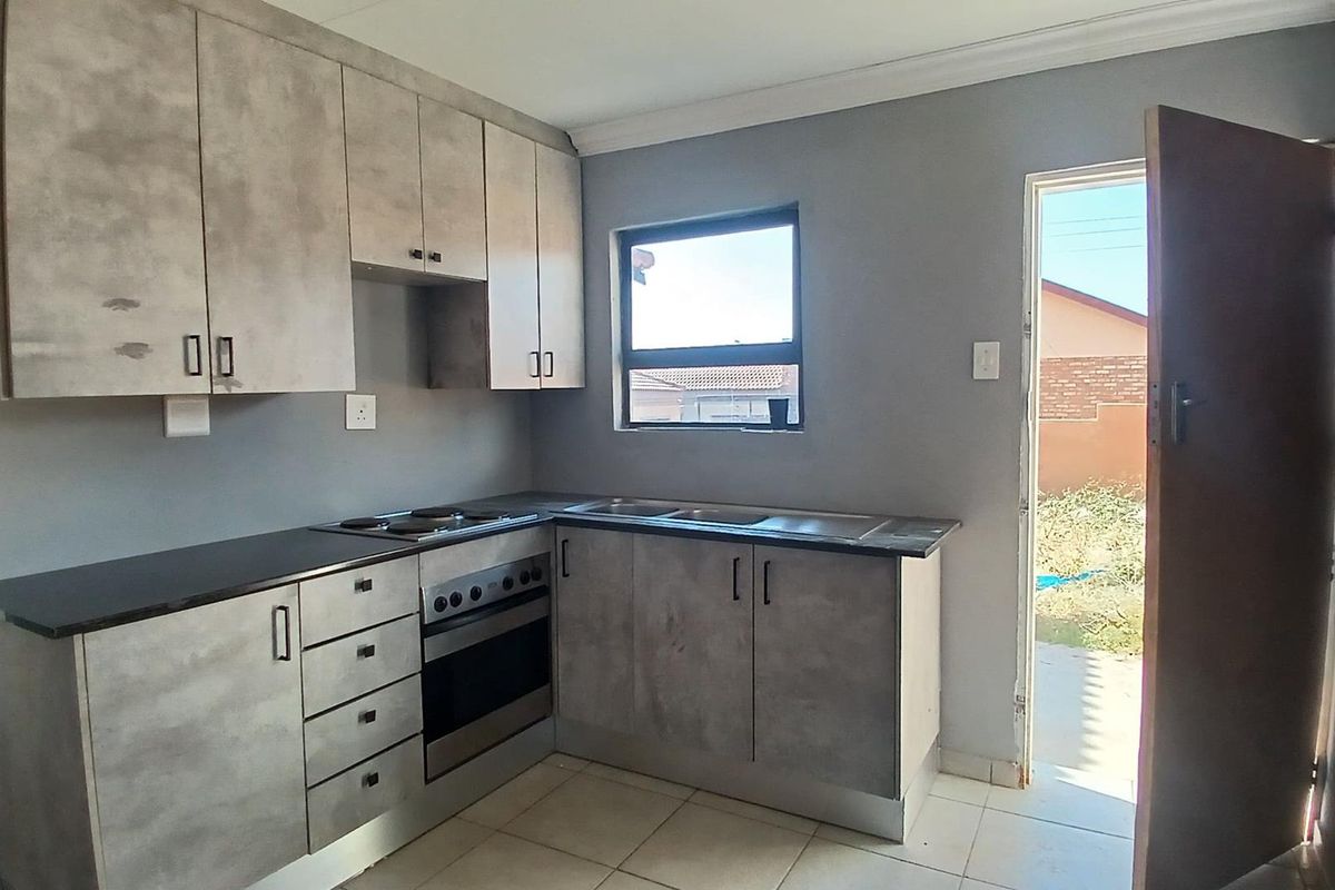 A functional kitchen featuring grey cabinetry, built-in oven and hob, stainless steel sink, and tiled flooring with direct access to the exterior.