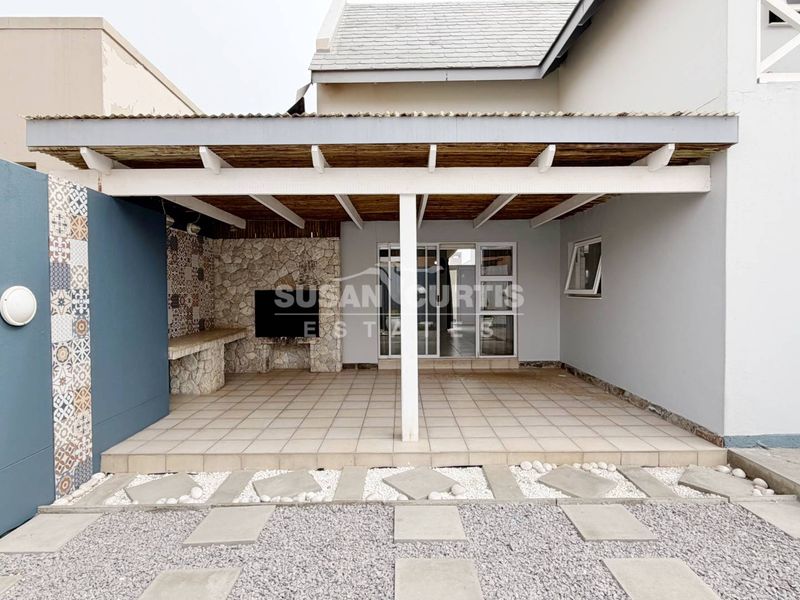 A covered outdoor patio featuring a built-in braai with stone cladding, tiled flooring, and direct access to the interior through sliding glass doors.