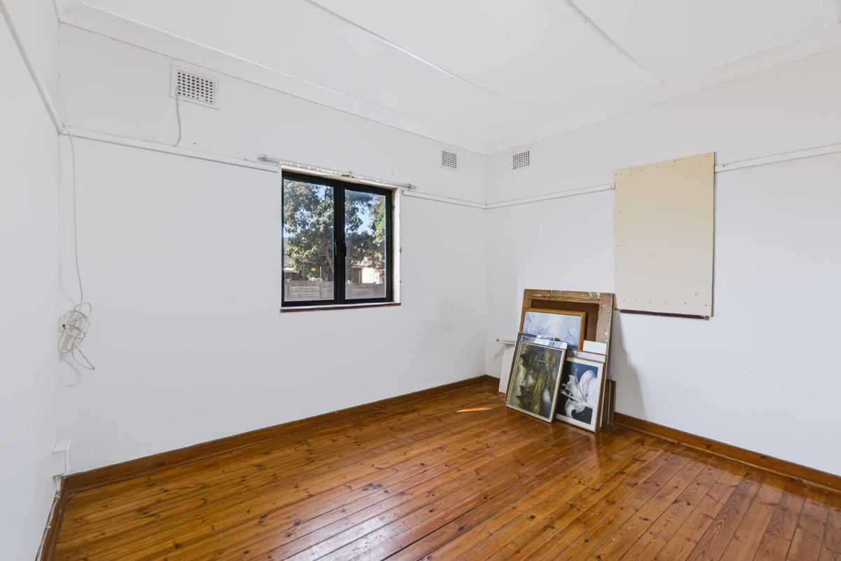 A vacant bedroom featuring original timber flooring, white walls, and a window, offering a blank canvas for renovation or interior design updates.