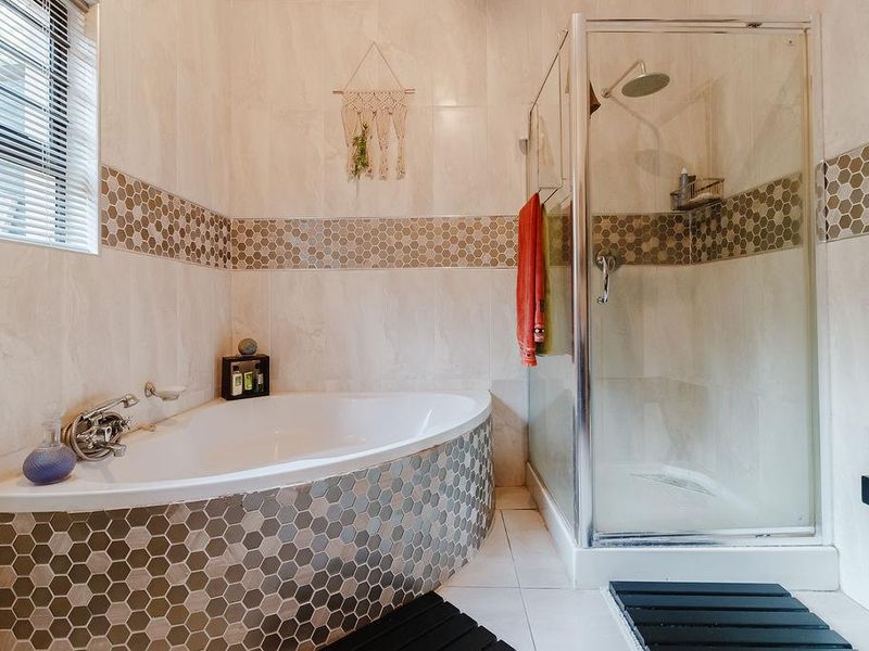 A well-maintained bathroom featuring a corner bathtub, a separate glass-enclosed shower, and decorative hexagonal tile accents.