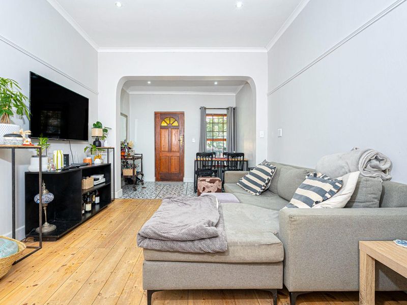 A bright living room featuring original hardwood flooring, a classic archway leading to the entrance, and decorative tiled flooring in the foyer area.