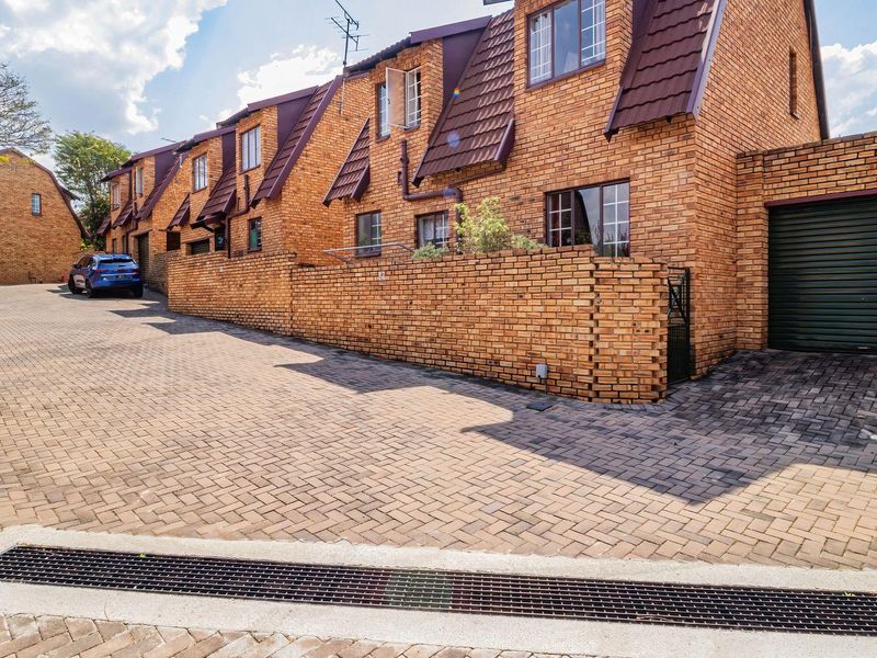 Front exterior view of a face brick townhouse complex featuring a paved driveway, private garage access, and secure boundary walling.