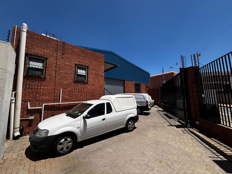 Rear exterior view of the industrial property featuring a face brick facade, secure metal roller shutter door, and paved driveway with perimeter security fencing.