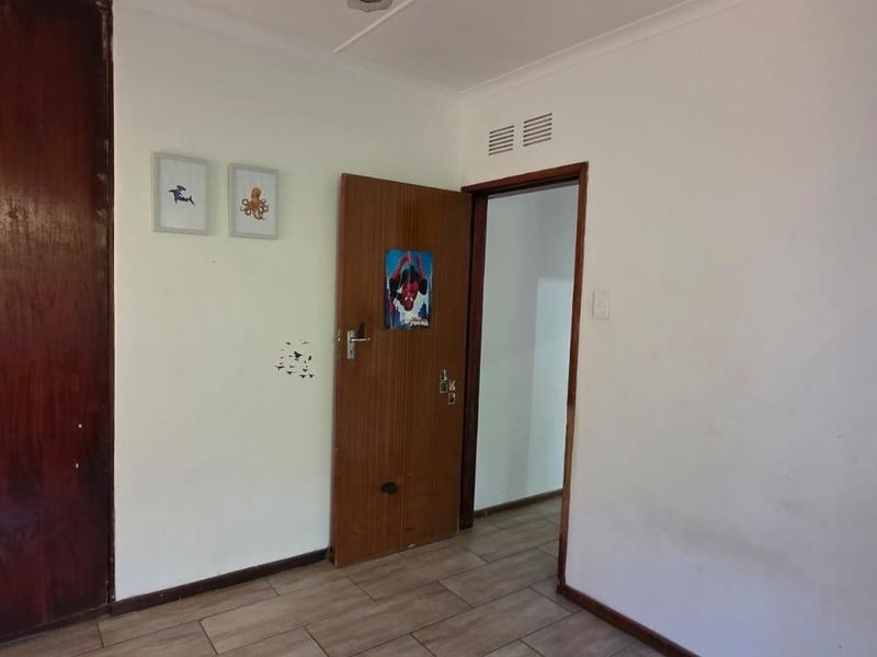 A bedroom featuring tiled flooring, a built-in wooden wardrobe, and a doorway leading to an adjacent space.