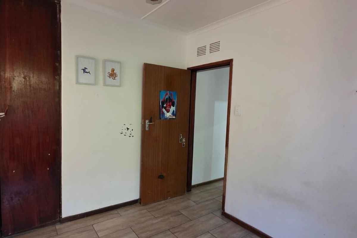 A bedroom featuring tiled flooring, a built-in wooden wardrobe, and a doorway leading to an adjacent space.