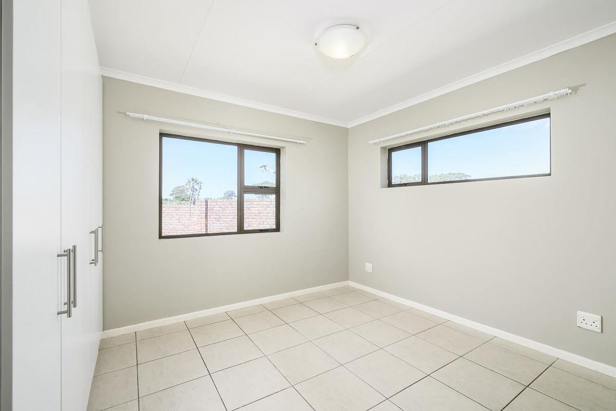 A bright, empty bedroom featuring neutral wall tones, tiled flooring, and built-in white cabinetry with modern hardware.