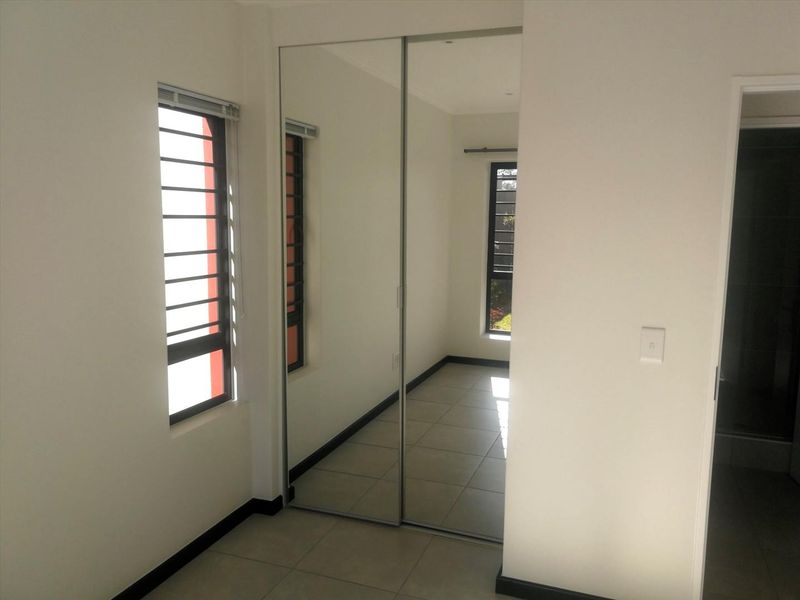 A bright, empty bedroom featuring tiled flooring, a large mirrored sliding wardrobe, and windows fitted with security bars.