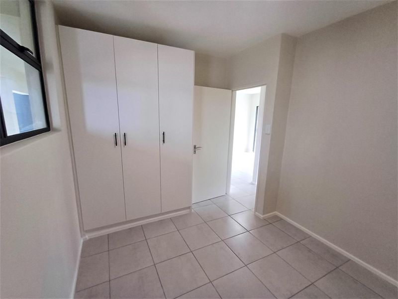 A clean, empty bedroom featuring neutral tiled flooring and modern white built-in cupboards, offering a bright and versatile living space.