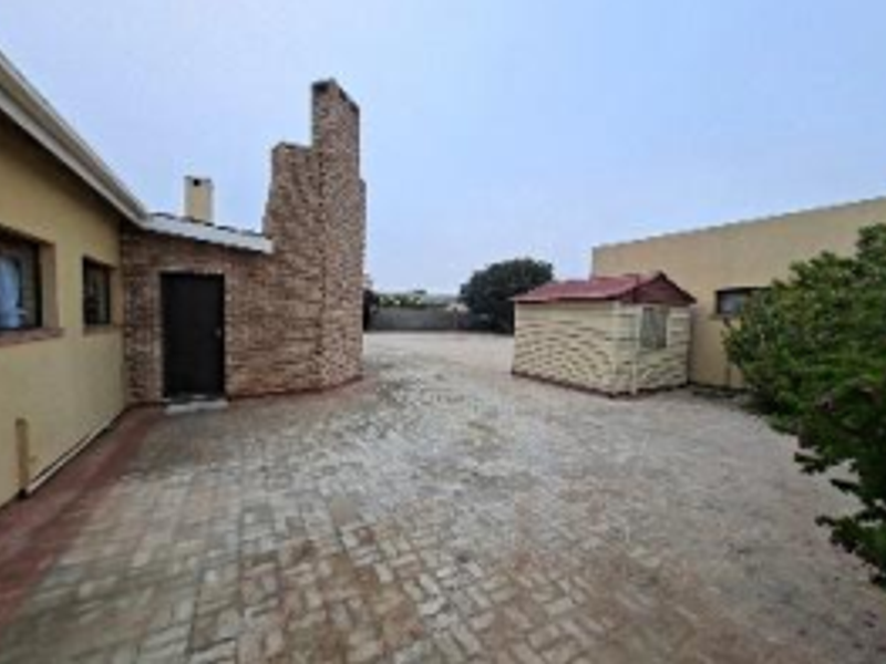 Rear exterior view of the property featuring a paved courtyard, brick chimney stack, and access to the main building.