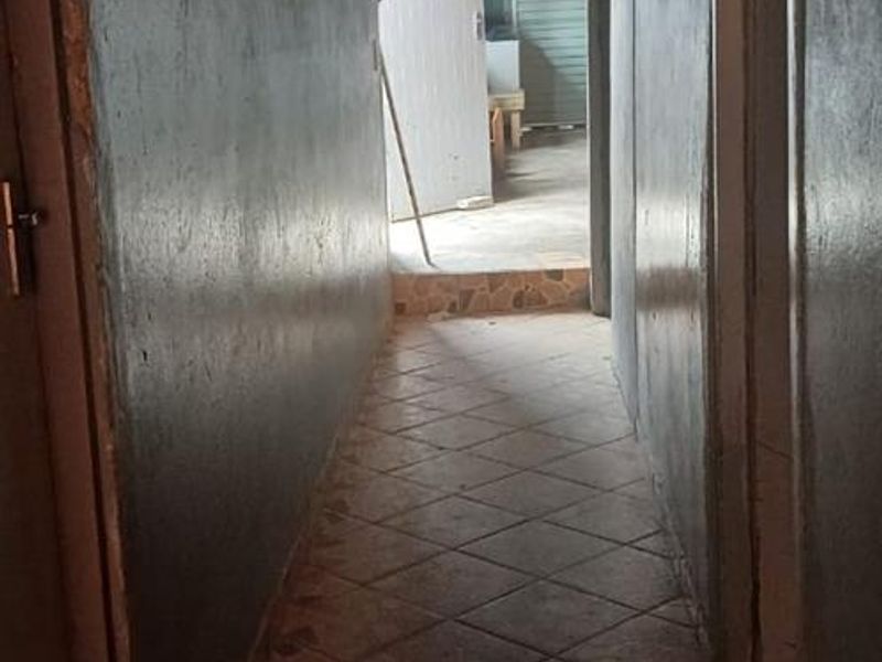 A narrow interior hallway featuring tiled flooring and an exposed beam ceiling, leading towards an exterior doorway.