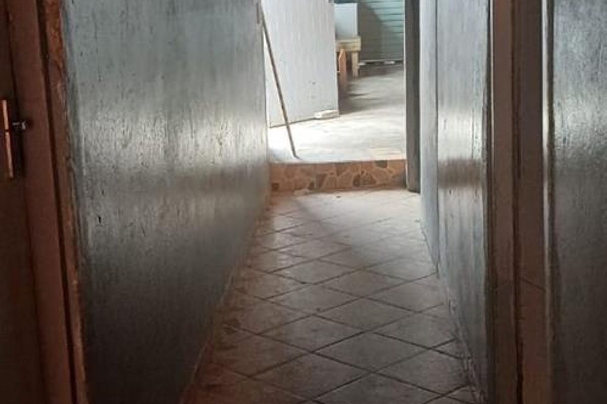 A narrow interior hallway featuring tiled flooring and an exposed beam ceiling, leading towards an exterior doorway.