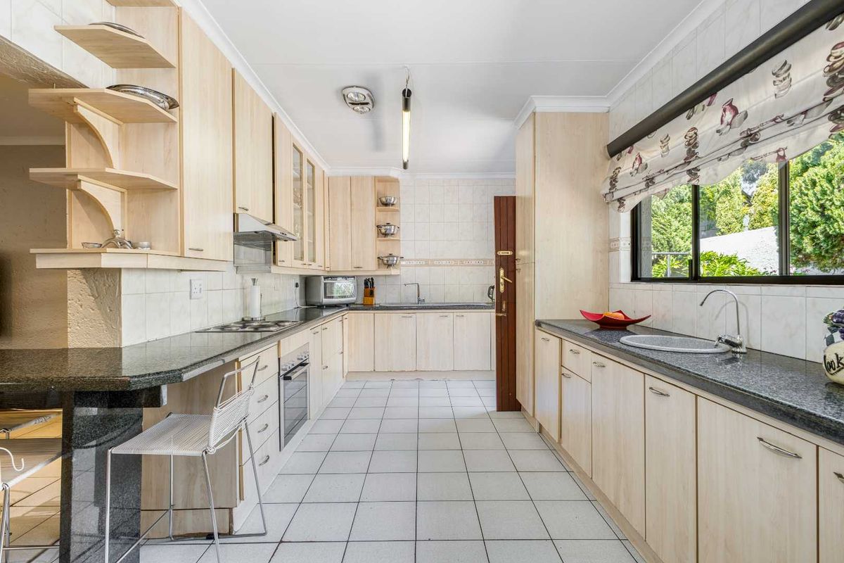 Functional kitchen featuring light wood cabinetry, granite countertops, tiled flooring, and a built-in oven and hob, offering ample storage and workspace.