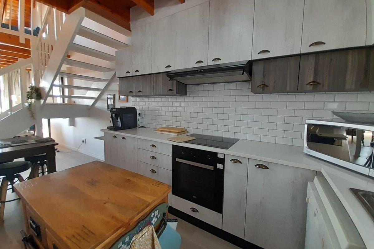 Modern kitchen featuring white cabinetry, subway tile backsplash, built-in oven, and hob, adjacent to an open staircase in a bright, contemporary apartment setting.