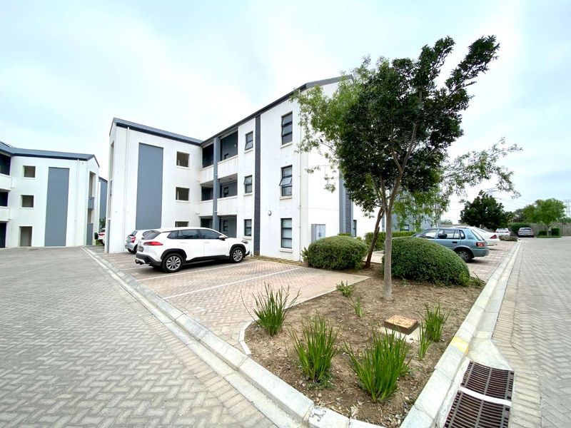 Exterior view of a modern apartment complex featuring paved parking bays and landscaped garden areas.