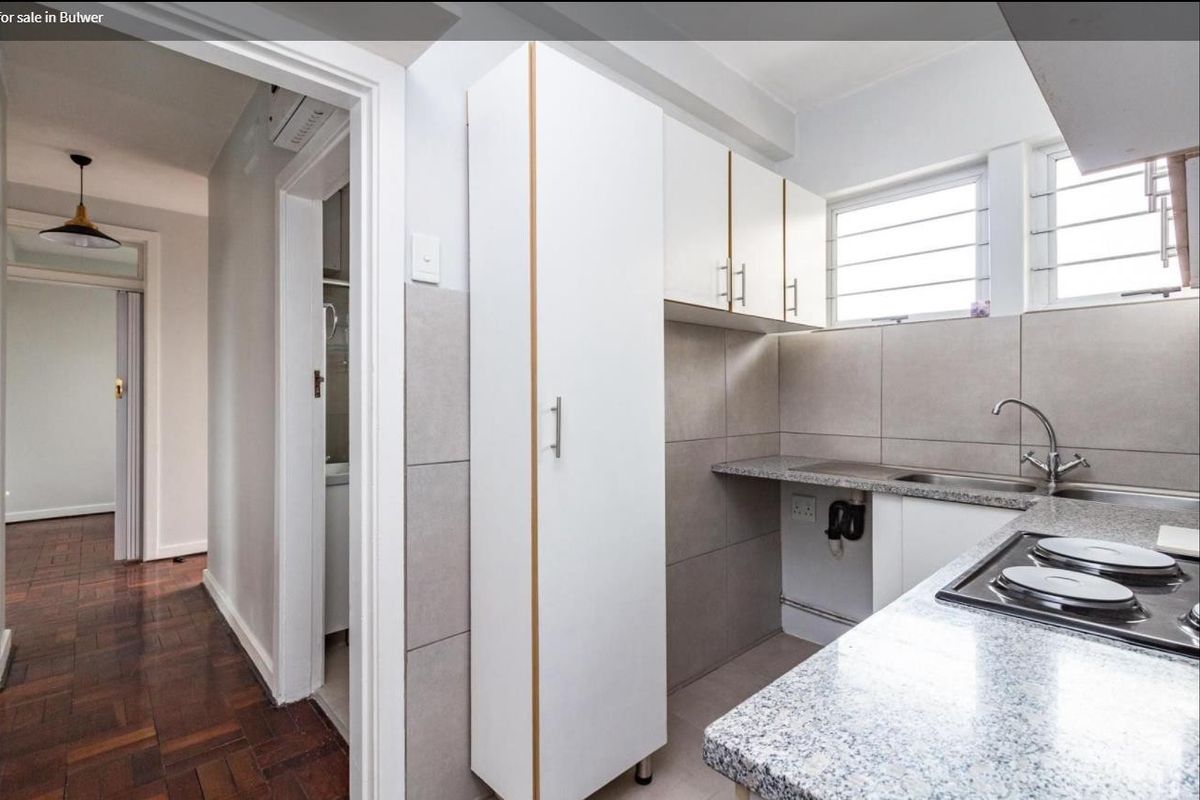 A clean, functional kitchen featuring modern white cabinetry, granite countertops, a built-in hob, and neutral tiled finishes.