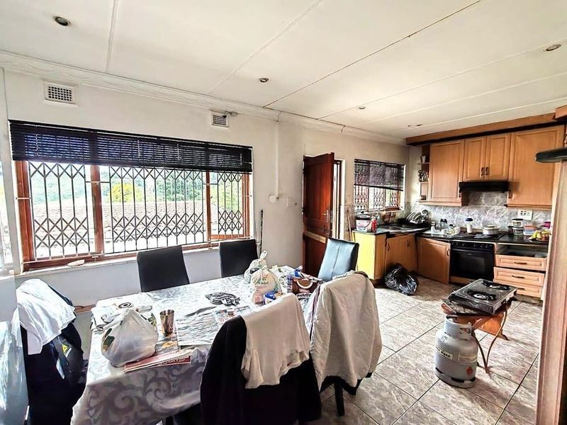 Open-plan kitchen and dining area featuring wooden cabinetry, built-in oven, extractor fan, and tiled flooring with security bars on windows.