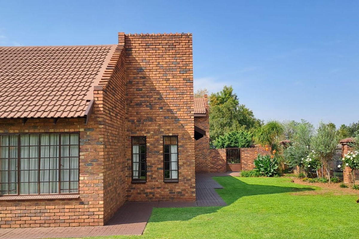 A well-maintained rear exterior view of a face brick house featuring a tiled roof, paved pathways, and a neat, landscaped garden.