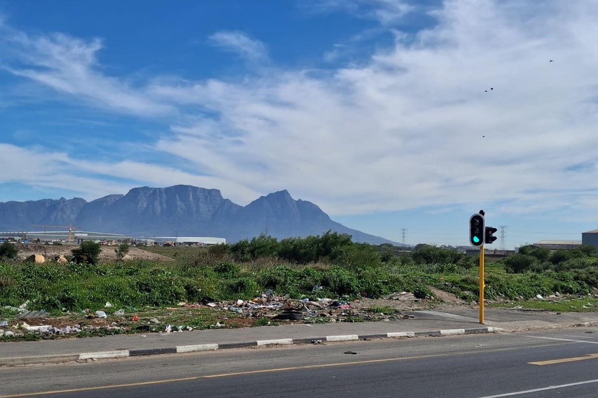 A view of vacant agricultural land from the roadside, featuring mountain vistas and a traffic light in the foreground.