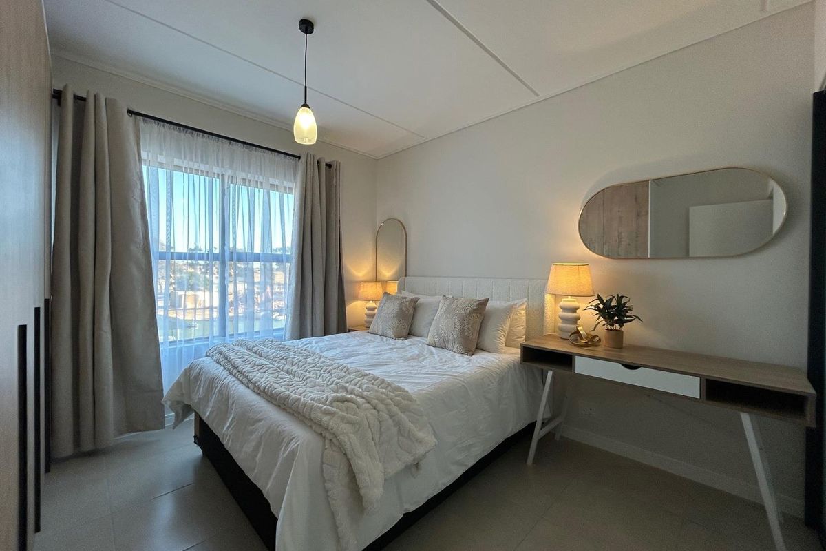 A well-lit bedroom featuring neutral tones, tiled flooring, built-in cabinetry, and large windows with sheer curtains, creating a comfortable and inviting living space.