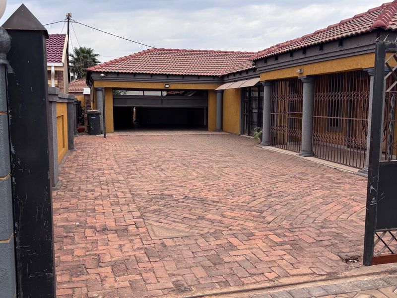 Front view of the property featuring a paved driveway, double garage, and secure gated entrance with security bars on the windows.