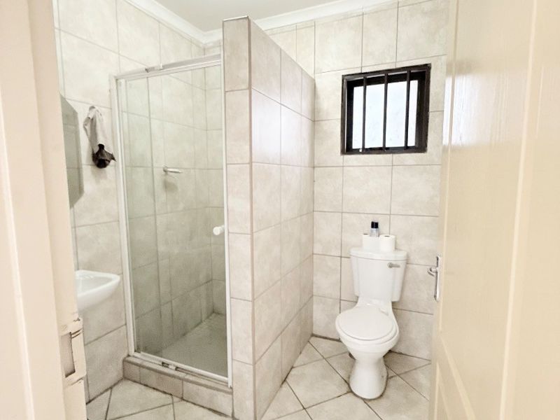 A functional bathroom featuring a tiled shower enclosure, toilet, and wall-mounted basin with neutral wall and floor tiles.